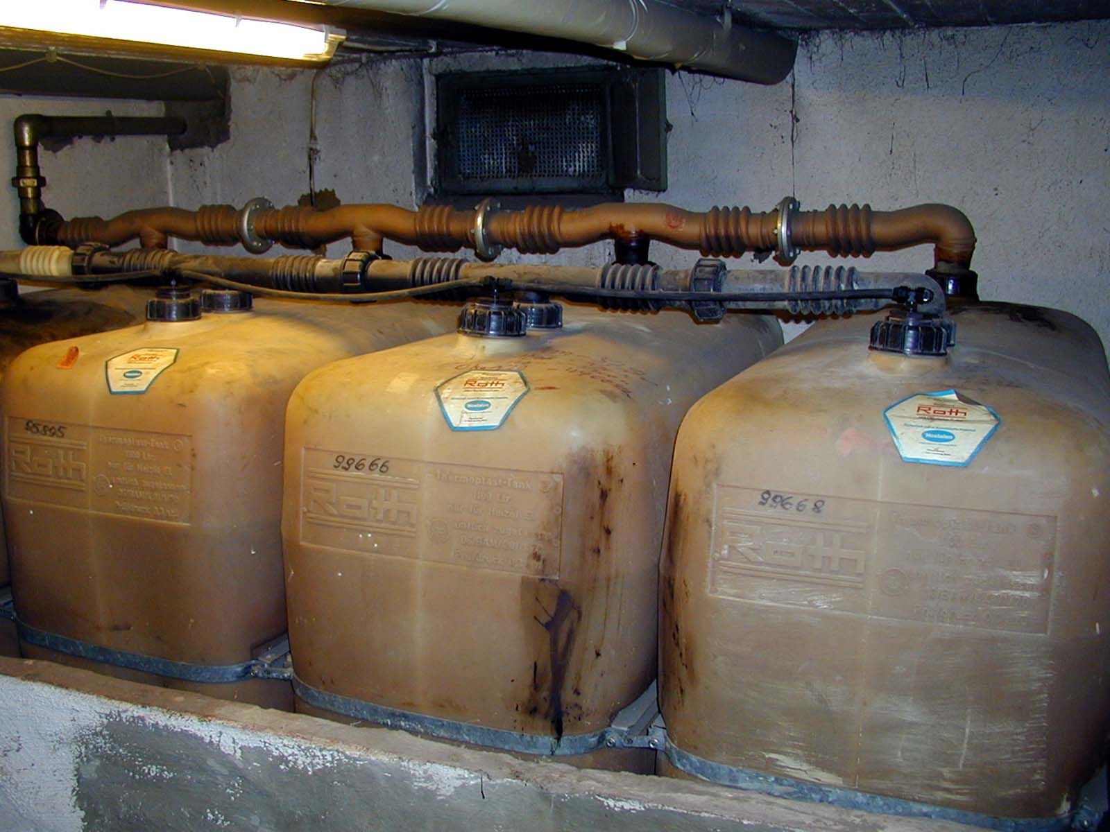 Three aging non-metallic oil tanks in a basement, stained and discoloured, joined by a fill manifold