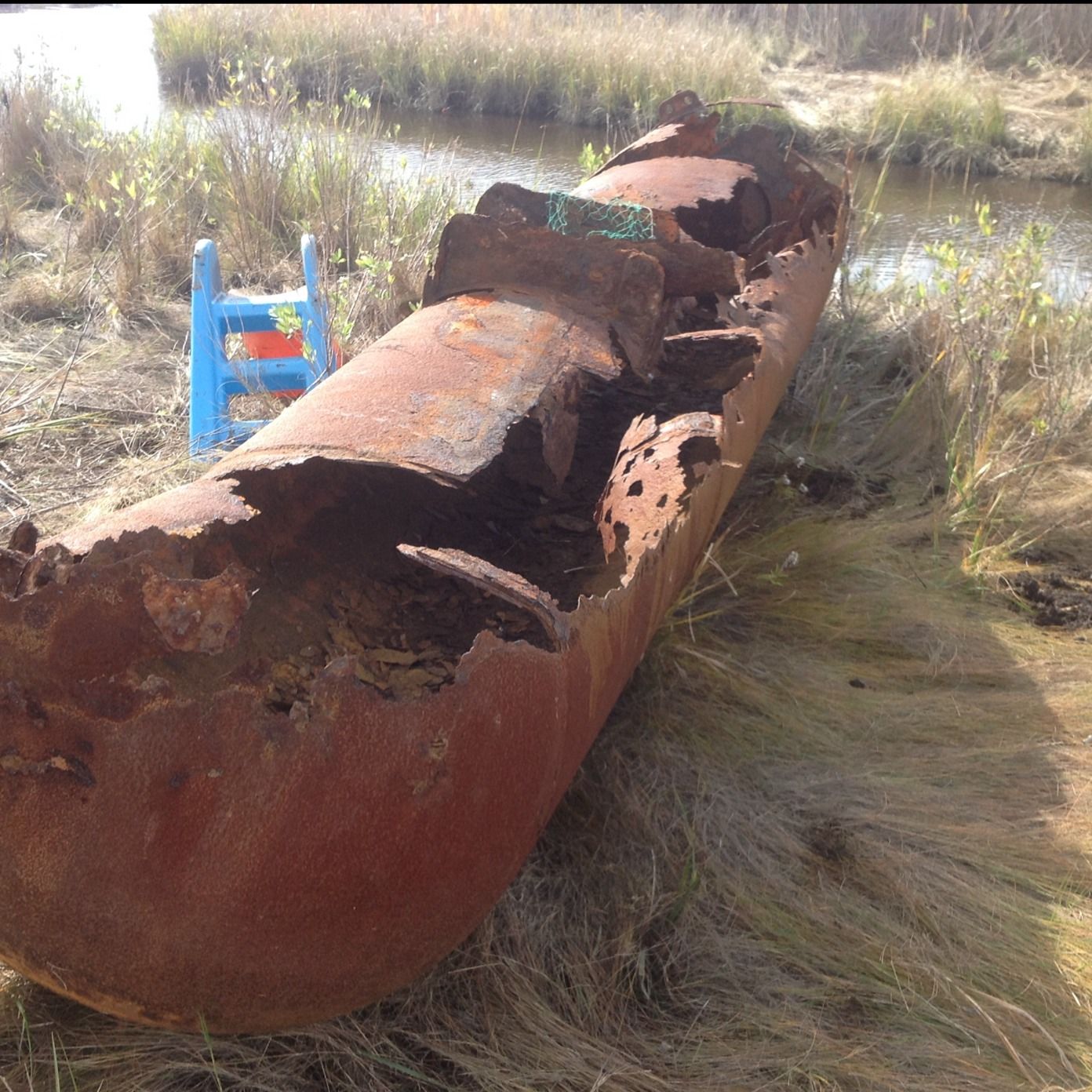 A badly rusted steel oil tank lying in the grass after being dug out and removed
